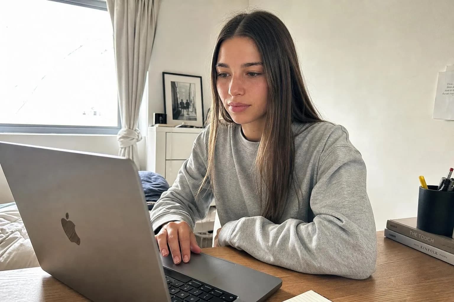 A character at a desk in daylight publishing a video from a laptop, checking the upload settings, an unposed candid rather than a staged shot