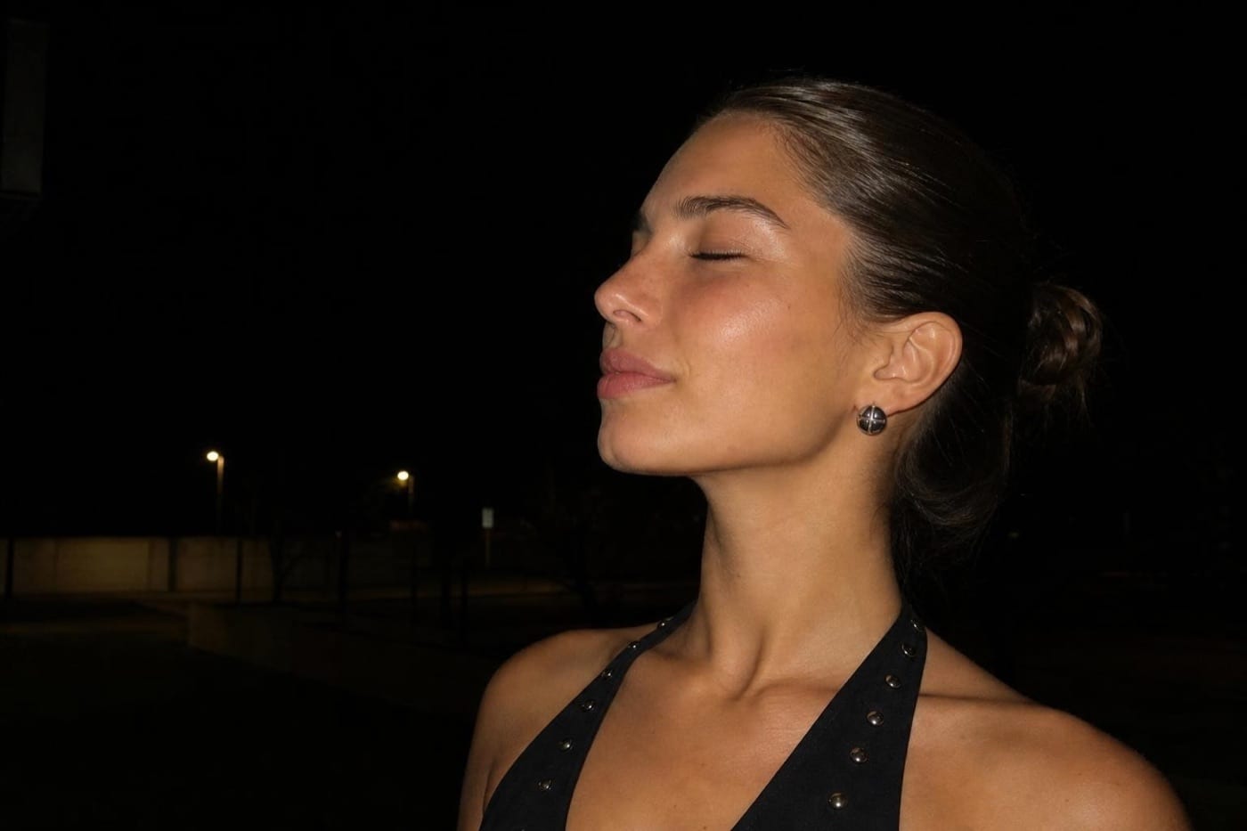 Candid night portrait of an AI character in profile, realistic skin texture under available street light, framed like a real phone photo rather than a studio render