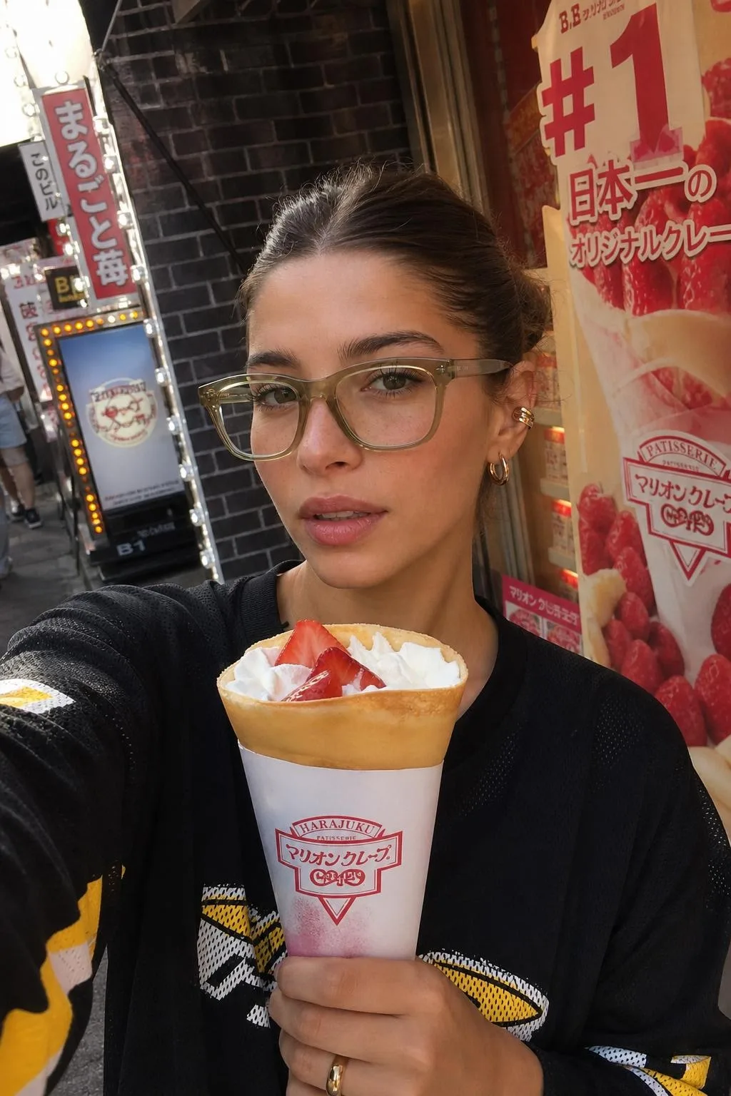 Same Cladegrove creator face placed on a Harajuku street in Tokyo in daylight, taking a candid selfie with a strawberry crepe in front of a patisserie, clear glasses and a black streetwear top
