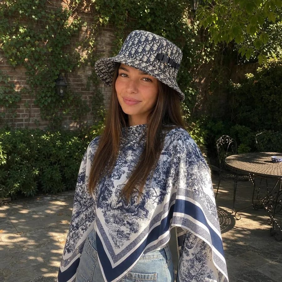 AI-generated Cladegrove result photo of a creator in a sunlit garden wearing a patterned bucket hat and toile scarf, the same locked face placed into a new scene