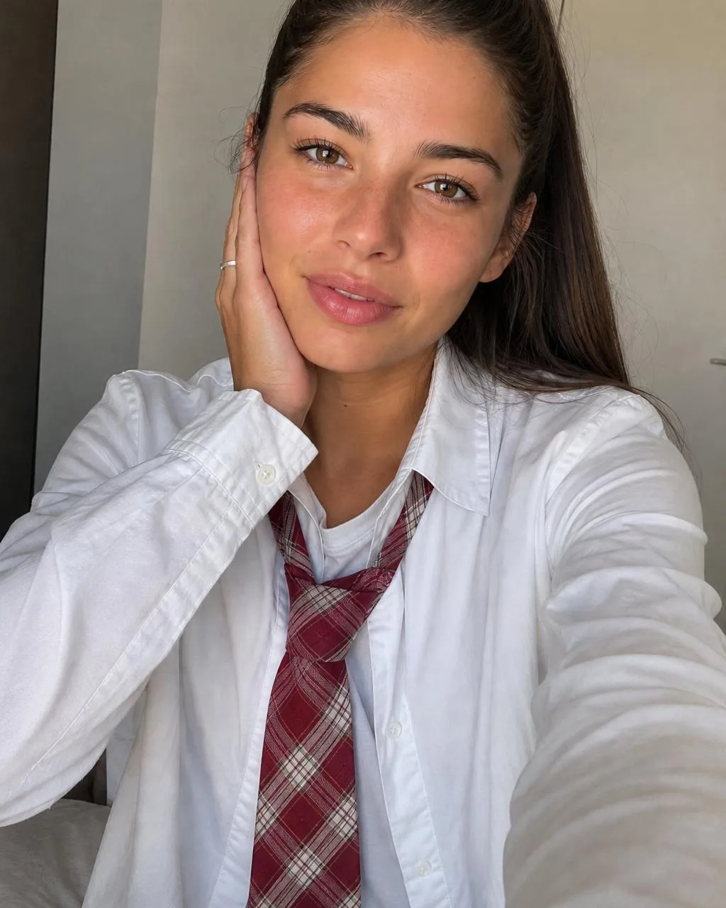 Cladegrove AI portrait of a young woman taking a no-makeup selfie in soft daylight, white shirt over a red plaid tie, real skin texture with natural freckles, fine grain and pores dosed where they belong, soft micro-highlights and credible depth. Same face stays across every photo on Cladegrove